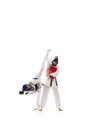 Two young girls in dobok and helmet training, practicing taekwondo poses, stances isolated over white background