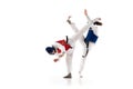 Two young girls in dobok and helmet training, practicing taekwondo poses, stances isolated over white background