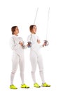 Two girls are fencers, in a uniform, holding swords and looking up at the sharp tip of the sword. Isolated. Royalty Free Stock Photo