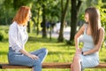 Two young girls friends sitting on a bench in summer park chatting happily having fun Royalty Free Stock Photo