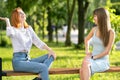 Two young girls friends sitting on a bench in summer park chatting happily having fun Royalty Free Stock Photo