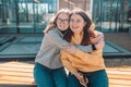 Two young girls friends smiling and hugging while sitting in a modern place looking at the camera Royalty Free Stock Photo