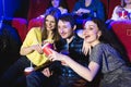 Two young girls and a guy watching a comedy in a cinema. Young friends watching movie in cinema. Group of people in Royalty Free Stock Photo