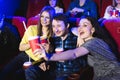 Two young girls and a guy watching a comedy in a cinema. Young friends watching movie in cinema. Royalty Free Stock Photo