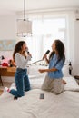 Two young girls holding brushes as microphones and singing songs on bed Royalty Free Stock Photo