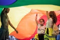 Two young girls and a man standing under a giant rainbow gay flag during the Belgrade Gay Pride.