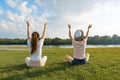 Two young girls meditate in the park near the river, back view, the girls raised their hands up, golden hour Royalty Free Stock Photo