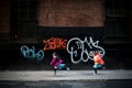 Two young girls running in front of graffiti in New York City street Royalty Free Stock Photo