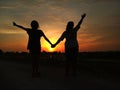 Two young girls silhouette holding hand having fun at sunset. Showing happiness, freedom and happy friendship.