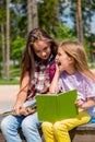 Two young girls sitting on the bench outdoors reading a book. Royalty Free Stock Photo