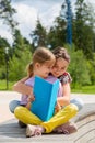 Two young girls sitting on the bench outdoors reading a book. Royalty Free Stock Photo