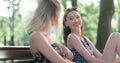 Two young girls sitting on bench in a park enjoying summer and chatting. Royalty Free Stock Photo