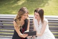 Two young girls sitting on a bench in a park watching the tablet and laughing Royalty Free Stock Photo