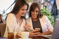 Two young girls sitting in cafe using smart phone. Royalty Free Stock Photo