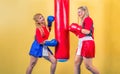 Two girls in tracksuits practice punching at a punching bag. Training young women in the gym.