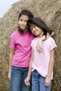 Two young girls standing by haybale