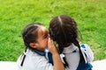 Two young girls whispering and sharing a secret during playground session on green glass background Royalty Free Stock Photo