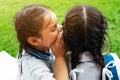 Two young girls whispering and sharing a secret during playground session on green glass background