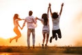 Two young guys and two girls are holding their hand and jumping in the field on a summer day. Back view. Royalty Free Stock Photo