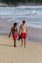 Two young guys walking along the coastline of ocean. Tourism of Asia. Australian and Asian teenagers on the beach. Royalty Free Stock Photo