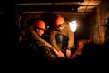 Two young guys in a working uniform and protective helmets, sitting in a low tunnel. Workers of the mine