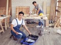 Two handsome Asian male repairmen or carpenters working together in wood workshop, one man sitting smiling and looking at camera