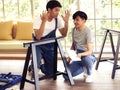 Two Asian men trying to assemble knockdown furniture and getting confused