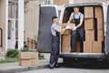 Two young handsome movers wearing uniforms are unloading the van full of boxes. House move, mover service