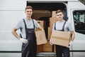 Two young handsome smiling workers wearing uniforms are standing next to the van full of boxes. House move, mover Royalty Free Stock Photo