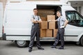 Two young handsome smiling workers wearing uniforms are standing next to the van full of boxes. House move, mover Royalty Free Stock Photo