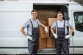 Two young handsome smiling workers wearing uniforms are standing next to the van full of boxes. House move, mover Royalty Free Stock Photo