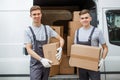 Two young handsome smiling workers wearing uniforms are standing next to the van full of boxes. House move, mover Royalty Free Stock Photo