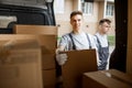 Two young handsome workers wearing uniforms are standing next to the van full of boxes. House move, mover service Royalty Free Stock Photo