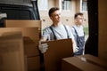 Two young handsome workers wearing uniforms are standing next to the van full of boxes. House move, mover service Royalty Free Stock Photo