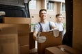 Two young handsome workers wearing uniforms are standing next to the van full of boxes. House move, mover service Royalty Free Stock Photo