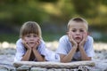 Two young happy cute blond children, boy and girl, brother and sister laying on pebbled beach on blurred bright sunny summer day Royalty Free Stock Photo