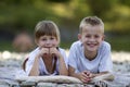 Two young happy cute blond children, boy and girl, brother and sister laying on pebbled beach on blurred bright sunny summer day Royalty Free Stock Photo