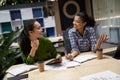 Two young and happy female coworkers sitting at the desk in the modern office and discussing project, working together Royalty Free Stock Photo