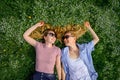 Two young happy women in a flowery meadow on sunny day, top view, close-up. Cheerful female friends lying on the lawn, looking at