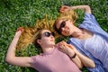 Two young happy woman on green grass outdoor. Romantic girls lying on the flowering meadow and holding hands. Serenity, youth,