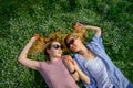 Two young happy woman on green grass outdoor. Romantic girls lying on the flowering meadow and holding hands. Serenity, youth,