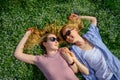 Two young happy woman on green grass outdoor. Romantic girls lying on the flowering meadow and holding hands. Serenity, youth,