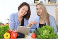 Two young happy women making online shopping for making menu by tablet computer. Friends cooking in the kitchen Royalty Free Stock Photo