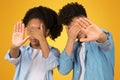 Two young individuals, a girl and a boy, playfully enact 'see no evil' with hands over eyes