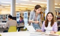 Two young interested women using laptop and books in library