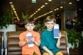 Two young kids sitting on brown chairs, holding passports and tickets in waiting hall in airport. Travel and holidays with Royalty Free Stock Photo