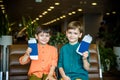 Two young kids sitting on brown chairs, holding passports and tickets in waiting hall in airport. Travel and holidays with Royalty Free Stock Photo