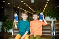 Two young kids sitting on brown chairs, holding passports and tickets in waiting hall in airport. Travel and holidays with Royalty Free Stock Photo