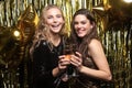 Two young ladies drinking champagne. Image of girls with balloons  on gold background Royalty Free Stock Photo