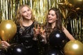 Two young ladies drinking champagne. Image of girls with balloons  on gold background Royalty Free Stock Photo